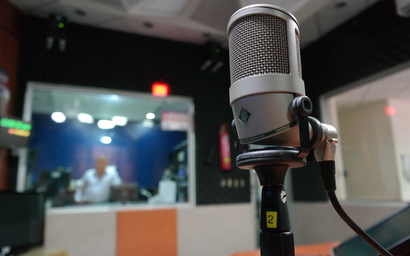 A presenter at the KPFA studio desk in Berkeley with a microphone and lit on-air sign